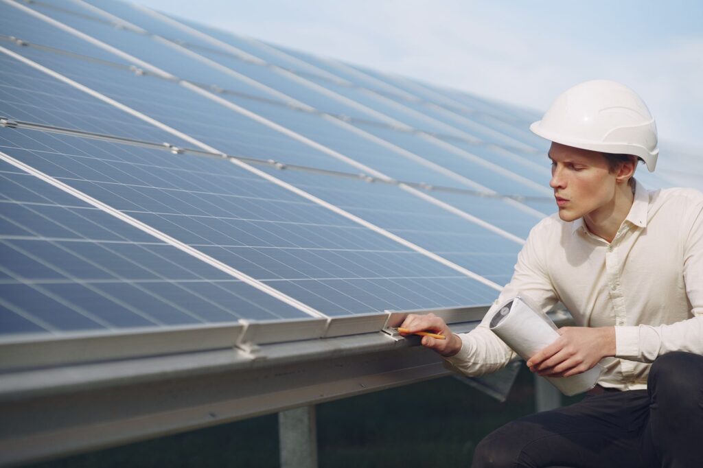 Focused young male employer in formal wear and hardhat working on solar panel station and checking d